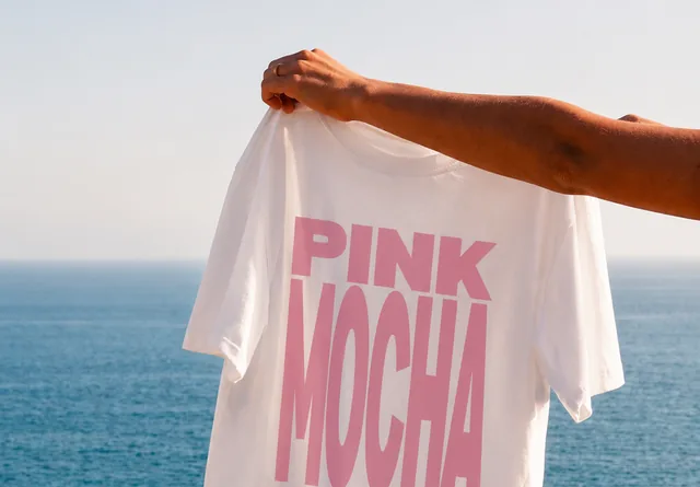 The Pink Mocha tee held up over the sea
