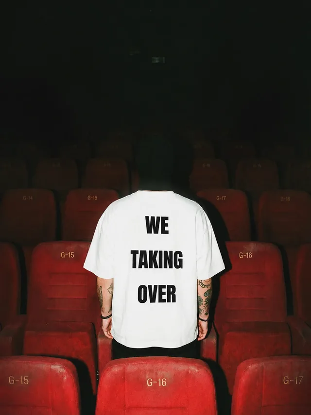 A bag-head in cinema seats, the WE TAKING OVER print on the back