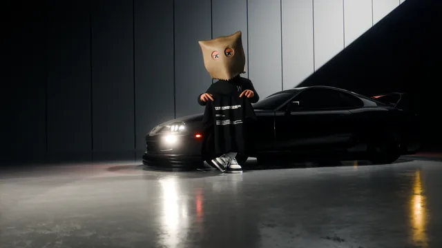 An ASM bag-head holds up THE DESIGNER tee in a dark studio beside a black sports car